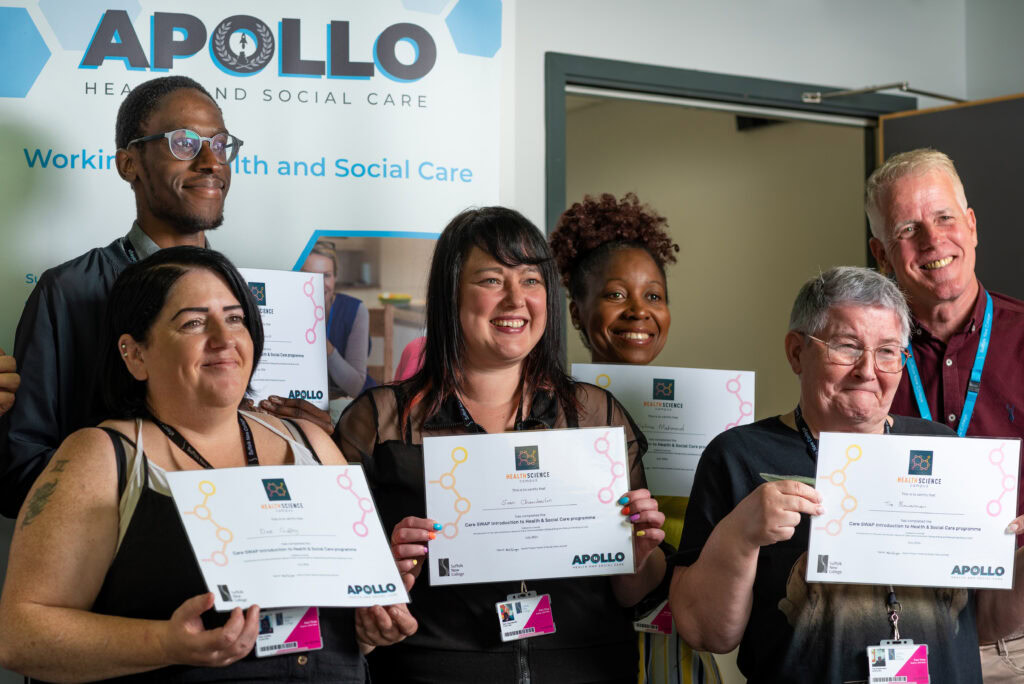 A group of people smiling gleefully while holding their course completion certificates. There is a white and blue banner behind them as a background.